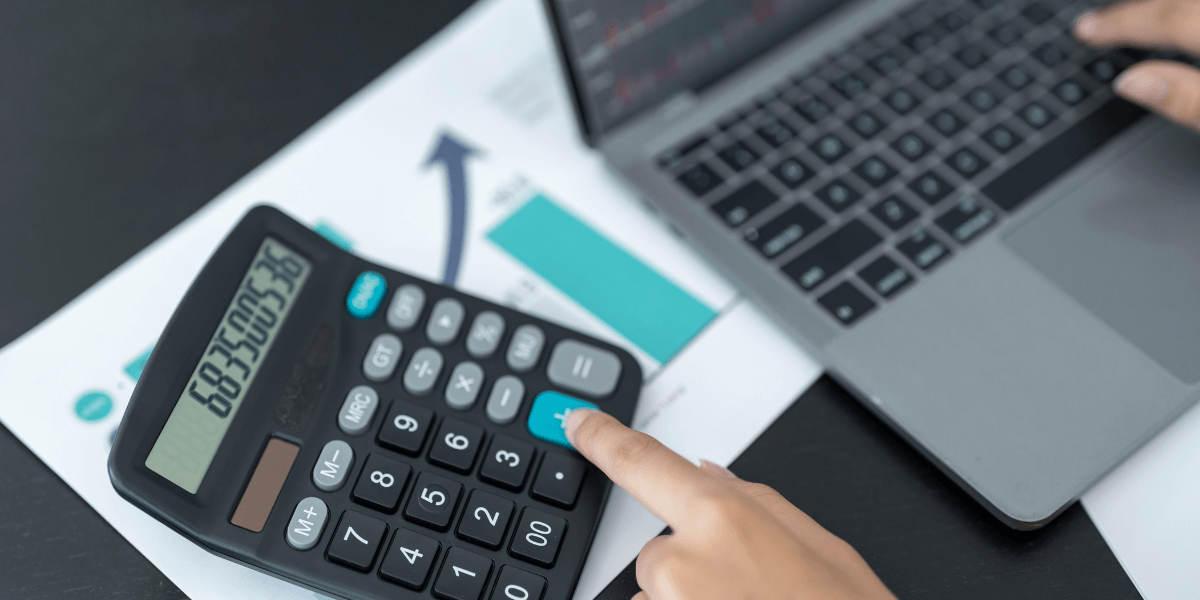 A person calculating costs using a calculator and laptop